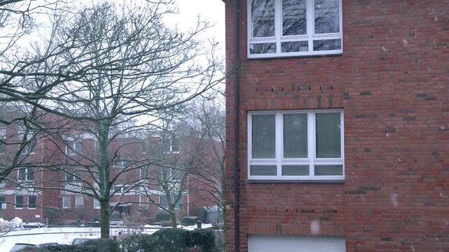 Red brick architectural apartment blocks in the background, snow falling in the foreground in slow motion.