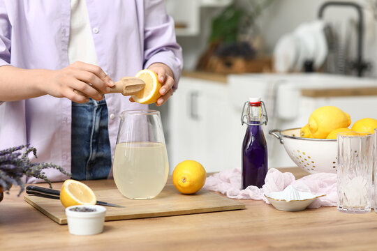 Young woman squeezing lemon for preparing lavender lemonade at table in kitchen
