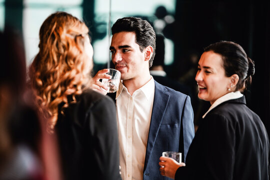 Professionals in formal attire networking at a corporate event, chatting and sipping drinks in a modern indoor setting.