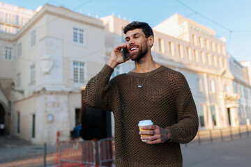 Handsome man on a Lisbon street talking on his phone with a coffee cup