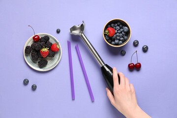 Female hand, blender and different berries on purple background