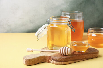 Jar and bowl of sweet honey with dipper on yellow table