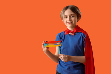 Cute little boy in superhero costume with graggers on orange background. Purim celebration