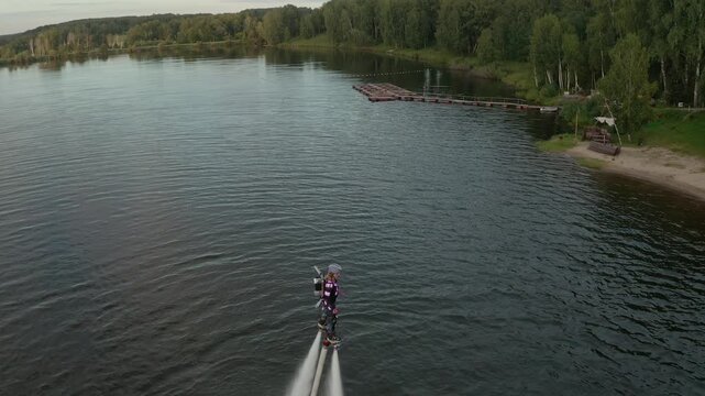 Flyboard show on open water. Athlete woman performs tricks in the air over a picturesque lake. Spectacular sports. Extreme lifestyle and water activity.