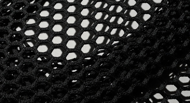 Close up of black oversized fishnet mesh fabric with a geometric hexagonal pattern against a light background creating sharp shadows and a detailed industrial textile texture