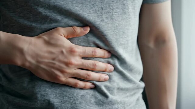 Close-up of a man holding his stomach in pain. Person clutching abdomen due to indigestion or ache. Health and medical concept