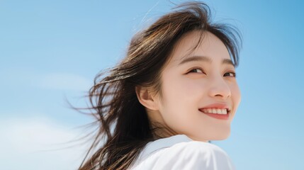 Fototapeta premium Happy young korean woman smiling against clear blue sky with wind in her hair.