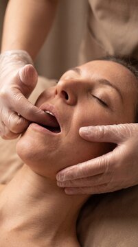 Woman receiving buccal facial massage, a beauty procedure for face sculpting. Rejuvenating cosmetic treatment on cheek and jawline.