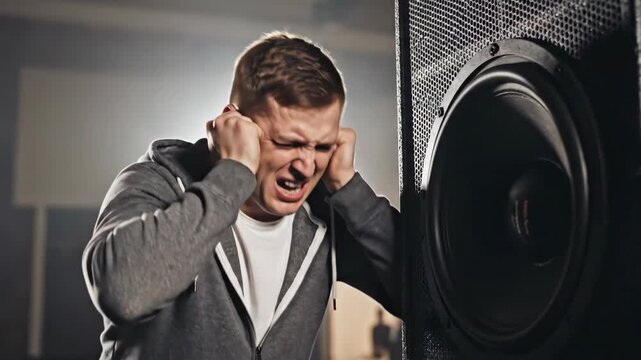 Man covering his ears in pain next to a loud speaker. Person grimacing from intense noise and high volume. Hearing protection and noise pollution concept