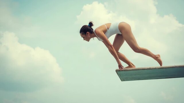 Athletic young woman in a white swimsuit poised on a diving board against a blue sky. Concept of summertime, outdoor sport, healthy lifestyle, and courage.