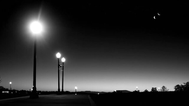 A grayscale night scene with streetlights illuminated against a gradient sky, and a crescent moon