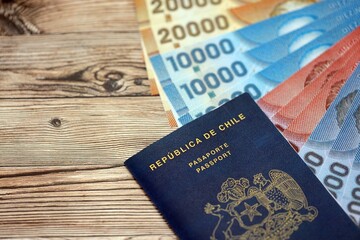 Chile Republic passport lies on wooden table with chilean pesos money bills close up. Chilean blue new passport book in details