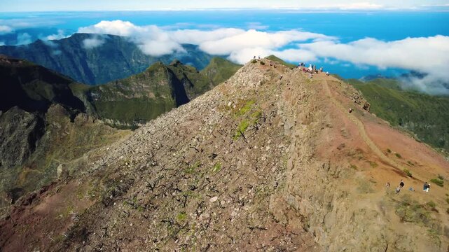 4K Aerial Orbit of Pico Ruivo Summit, Highest Peak of Madeira: Hikers Trekking on PR1.2 Trail, Majestic Volcanic Mountain Landscape, Dramatic Establishing Shot Above Clouds at Noon