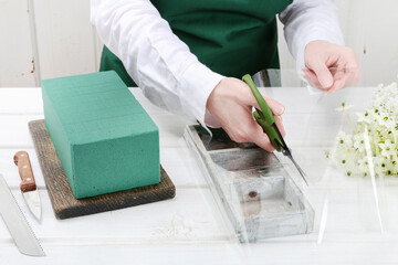 Florist at work: woman shows how to make Easter floral table decoration with arabian star flowers and gypsophila paniculata twigs in simple wooden box. Step by step, tutorial.