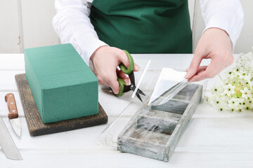 Florist at work: woman shows how to make Easter floral table decoration with arabian star flowers and gypsophila paniculata twigs in simple wooden box. Step by step, tutorial.