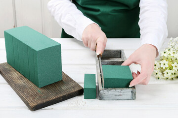 Florist at work: woman shows how to make Easter floral table decoration with arabian star flowers and gypsophila paniculata twigs in simple wooden box. Step by step, tutorial.