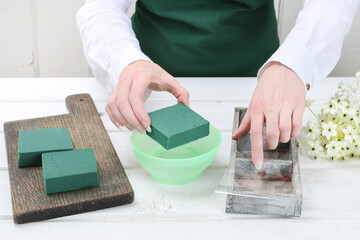 Florist at work: woman shows how to make Easter floral table decoration with arabian star flowers and gypsophila paniculata twigs in simple wooden box. Step by step, tutorial.