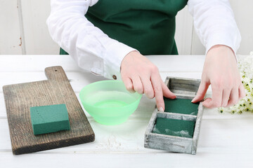 Florist at work: woman shows how to make Easter floral table decoration with arabian star flowers and gypsophila paniculata twigs in simple wooden box. Step by step, tutorial.