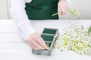 Florist at work: woman shows how to make Easter floral table decoration with arabian star flowers and gypsophila paniculata twigs in simple wooden box. Step by step, tutorial.