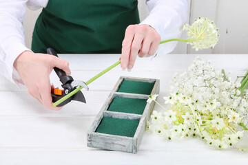 Florist at work: woman shows how to make Easter floral table decoration with arabian star flowers and gypsophila paniculata twigs in simple wooden box. Step by step, tutorial.