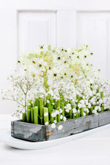 Florist at work: woman shows how to make Easter floral table decoration with arabian star flowers and gypsophila paniculata twigs in simple wooden box. Step by step, tutorial.