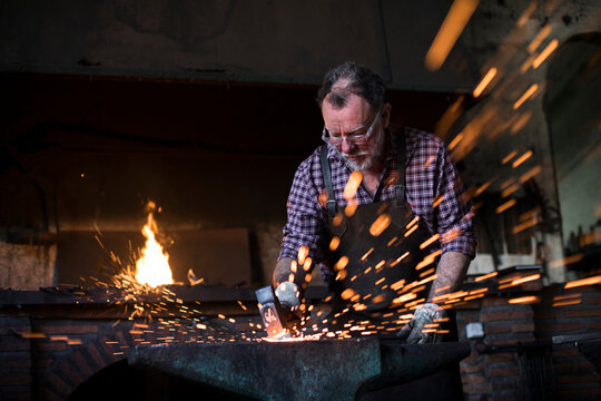 Blacksmith working with hammer at anvil in his workshop