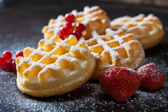 Waffles, strawberries and red currants sprinkled with icing sugar, close-up