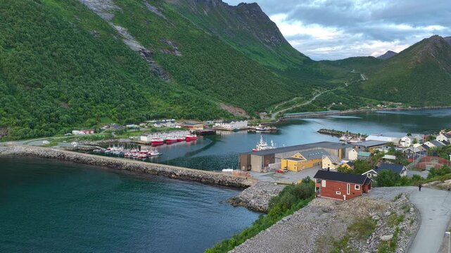 Aerial, forward drone flight, above Hus&oslash;y island and harbor. Fishing ships in harbor. Amazing wild nature during midnight sun in summer on Senja island in Norway. Beautiful landscape, wild nature. Fjo