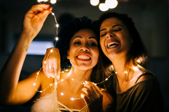 Close-up of cheerful female friends holding illuminated string lights at home