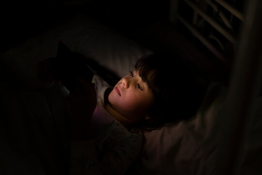 Girl lying in bed using smartphone at night