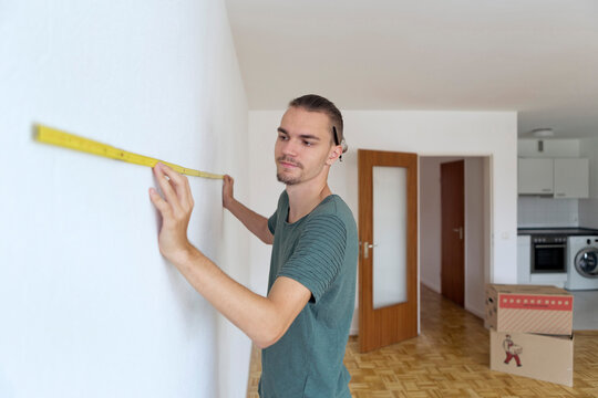 Young man measuring the wall in an empty apartment