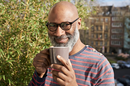 Mature amn standing on balcony, drinking coffee