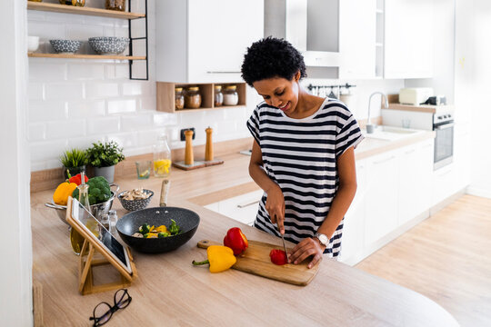 Young woman with tablet cooking in kitchen at home cutting vegetables