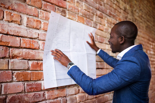 Smiling businessman studying plan at brick wall