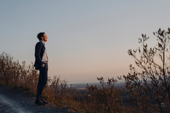 Mature businessman standing on a disused mine tip at sunset looking at view