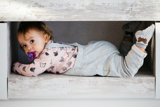 Portrait of baby girl with pacifier hiding at home