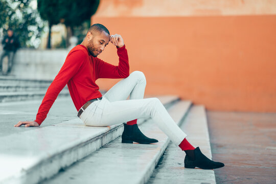 Fashionable young man wearing red pullover and socks sitting on stairs relaxing