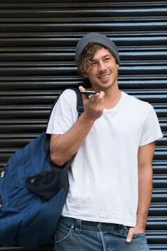 Smiling young man using cell phone at roller shutter