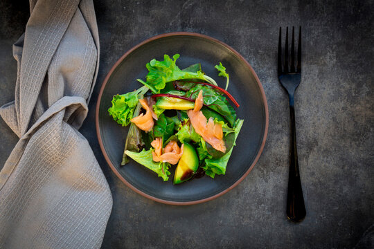 Plate of green salad with corn salad, arugula, spinach, red leaf lettuce, beetroot leaves, avocado, salmon meat and balsamic vinegar