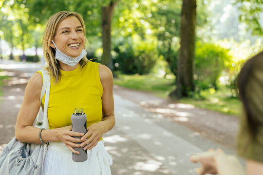 Two women meeting in nature with let down face masks