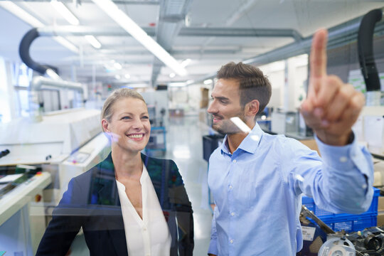 Young male technician pointing at graphical interface on glass in factory