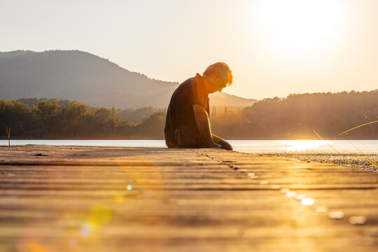 Senior man sitting on a wooden footbridge and looking down, against the sun