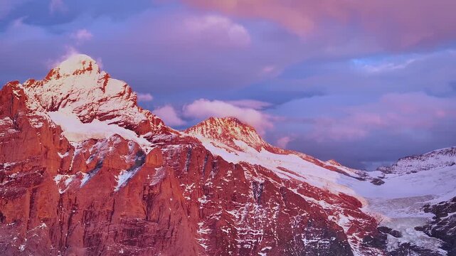 Aerial view of snow-covered mountain peaks and glaciers bathed in the warm glow of sunset, creating a stunning contrast with the cool sky, Grindelwald, Canton of Bern, Switzerland.