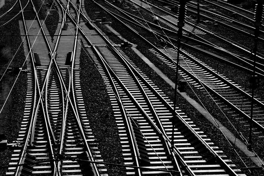 Parallel tracks at Hagen Central Station (Westphalia, Germany) in contrasting black and white. Numerous railroad tracks glisten in the sun, forming a complex system of switches, crossings, signals, an