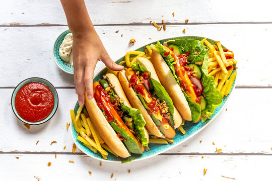 Hot dogs with french fries, ketchup and mayonnaise, hand taking an hot dog