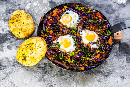 Pan of beetroot shakshouka with chard, carrots, tomatoes, red cabbage and pita bread
