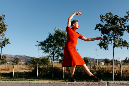 Non-binary male wearing red dress dancing on retaining wall