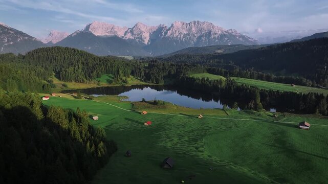 Aerial view of a serene lake reflecting the sky, nestled amidst verdant forests and majestic mountains under a soft, diffused light, Krun, Bavaria, Germany.