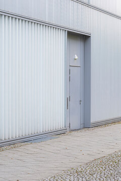 Minimal modern architecture showing a metal door on an urban sidewalk with a clean wall facade and simple exterior geometry in quiet daylight