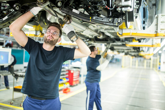 Two colleagues working at car underbody in modern factory
